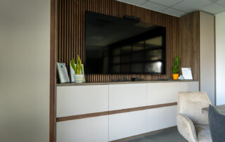 Moderne Medienwand mit Holzlamellen, Stauraumlösungen und integriertem Bildschirm im Besprechungsraum der Bremer GmbH.