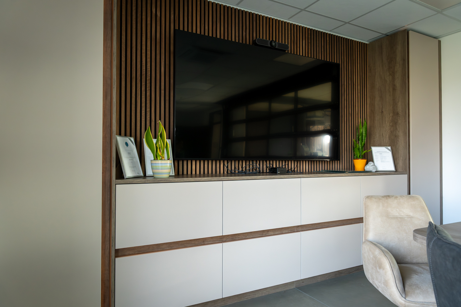Moderne Medienwand mit Holzlamellen, Stauraumlösungen und integriertem Bildschirm im Besprechungsraum der Bremer GmbH.